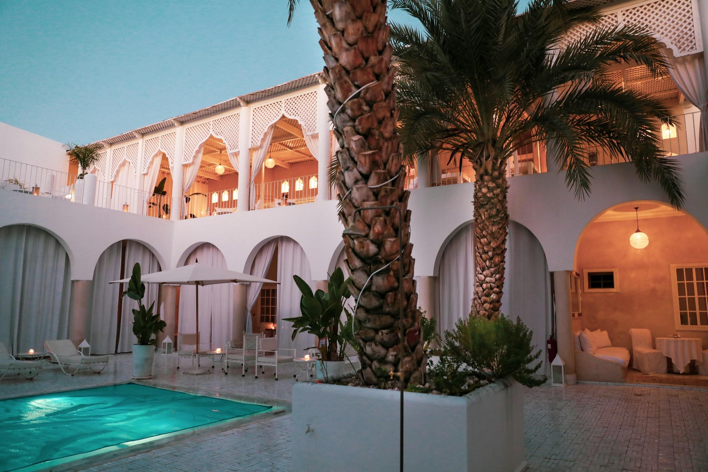 Pool at a Marrakech riad, white arches and palm trees at sunset